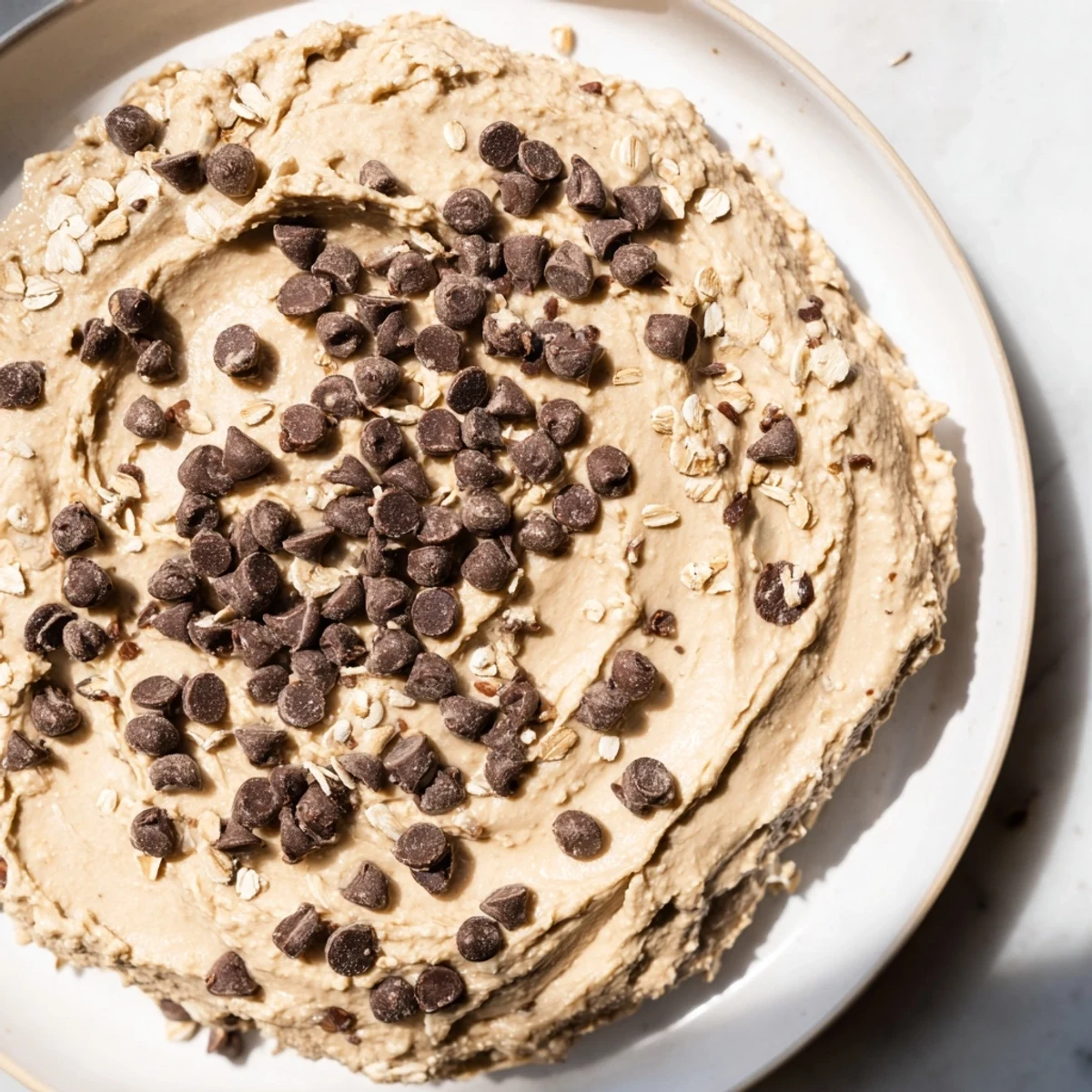 Creamy chocolate chip cookie dough hummus served in a bowl with crisp apple slices and pretzels for dipping.  