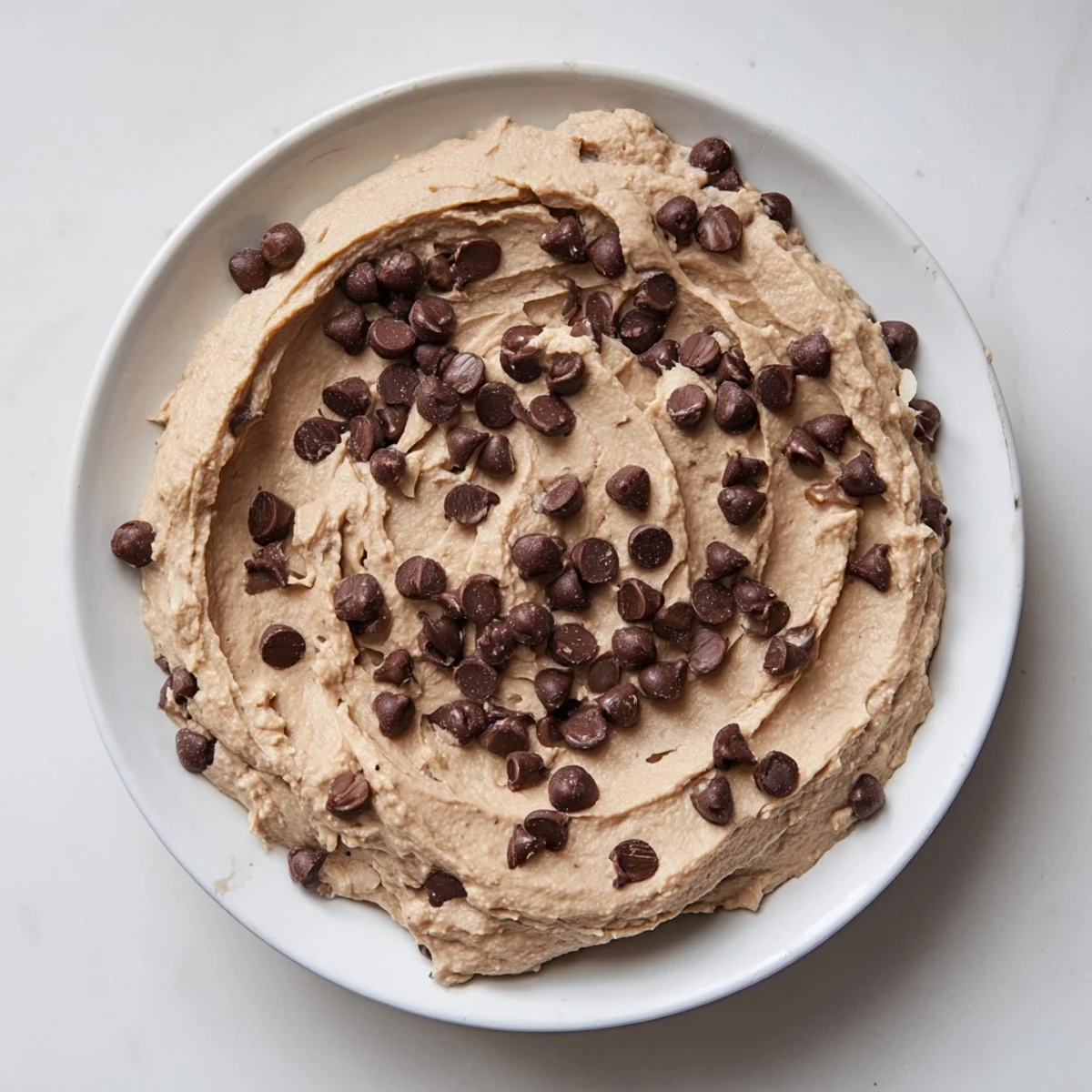 Homemade chocolate chip cookie dough hummus in a rustic dish, perfect for snacking or parties.