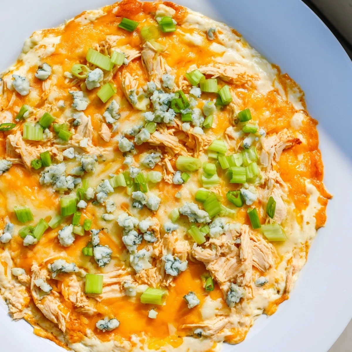 A close-up of creamy, gooey Spicy Buffalo Chicken Dip topped with blue cheese crumbles and chopped scallions.