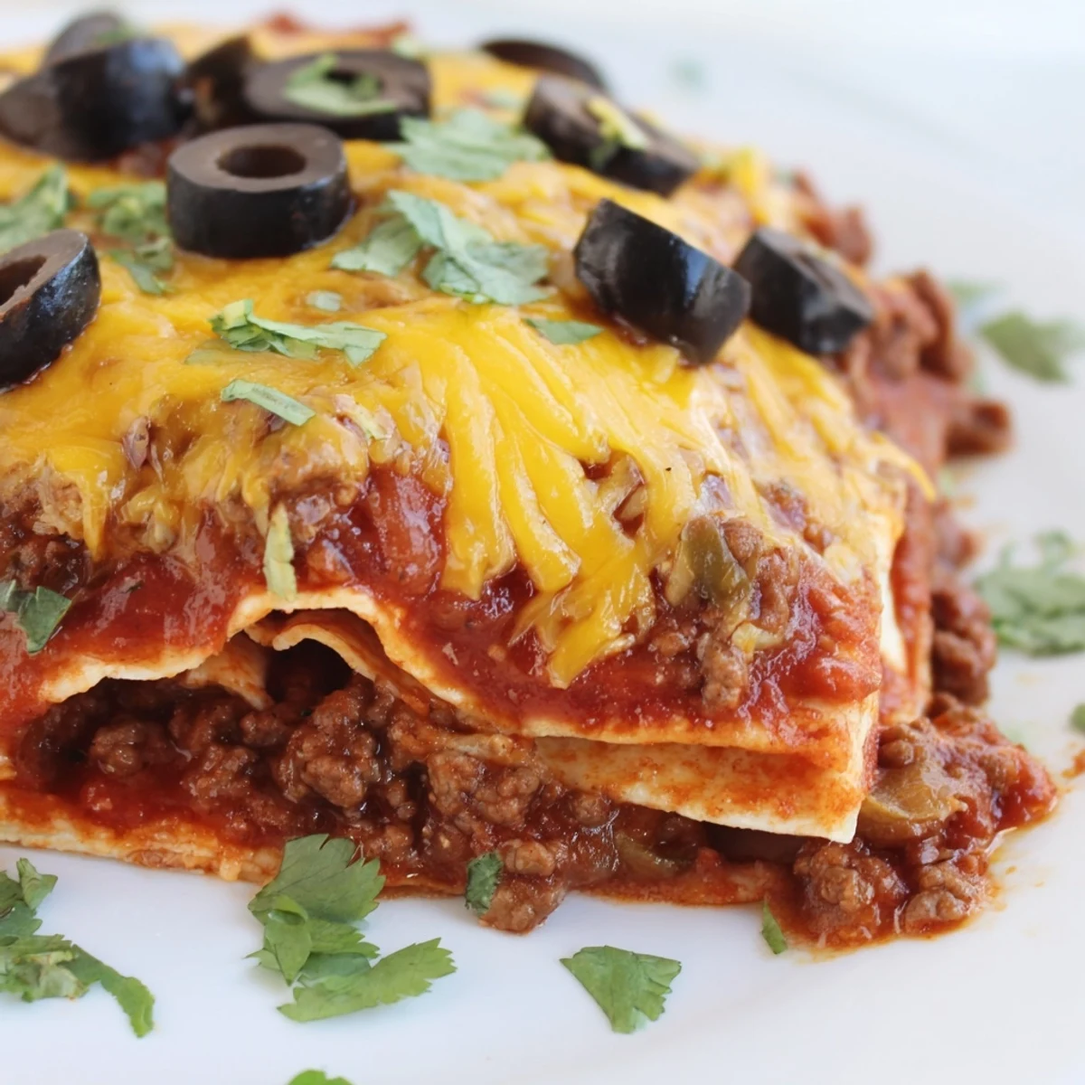 A close-up view shows the bubbly, golden-brown top of a freshly baked Tex-Mex Beef Enchilada Casserole served with a side of sour cream.