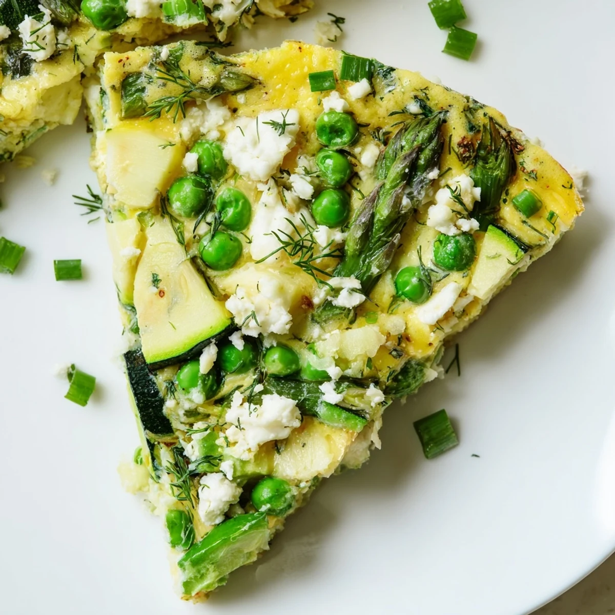 Spring vegetable frittata with herbs in a cast-iron skillet, topped with feta and fresh chives, ideal for a healthy meal.  