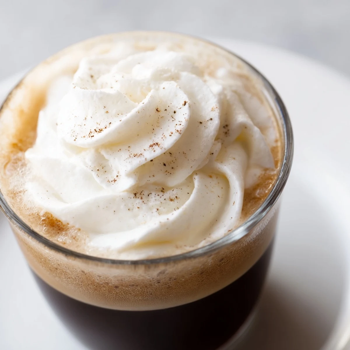 Two clear mugs of Irish Coffee Mocktail with Whipped Cream sit on a rustic table, steam rising from the dark coffee beneath the snowy cream topping.