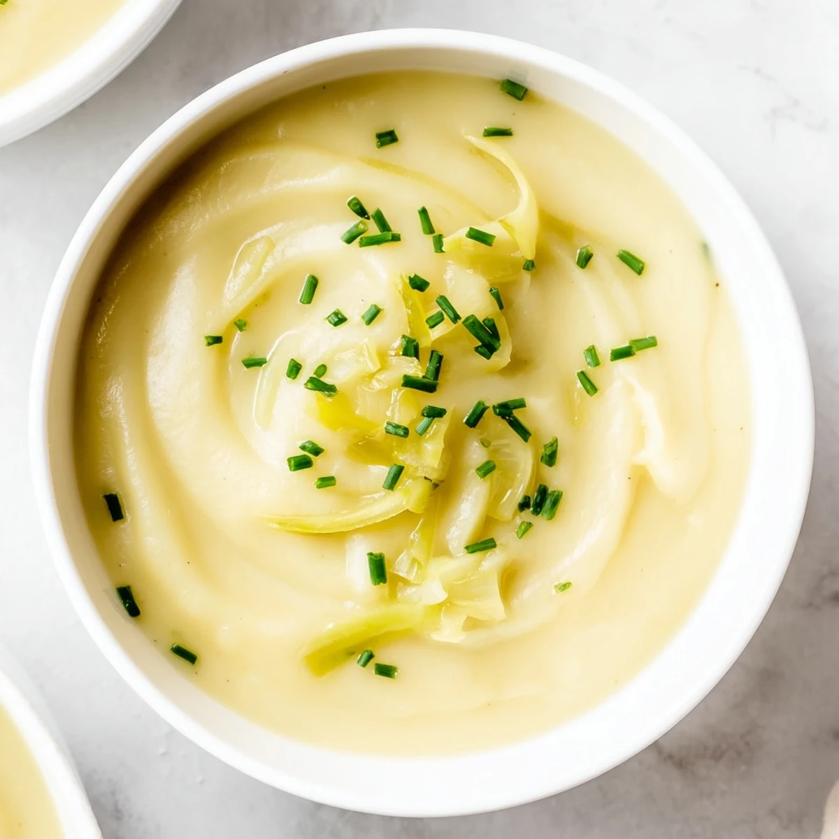 A close-up of velvety Creamy Potato Leek Soup with Chives, steaming gently and topped with finely minced green chives.