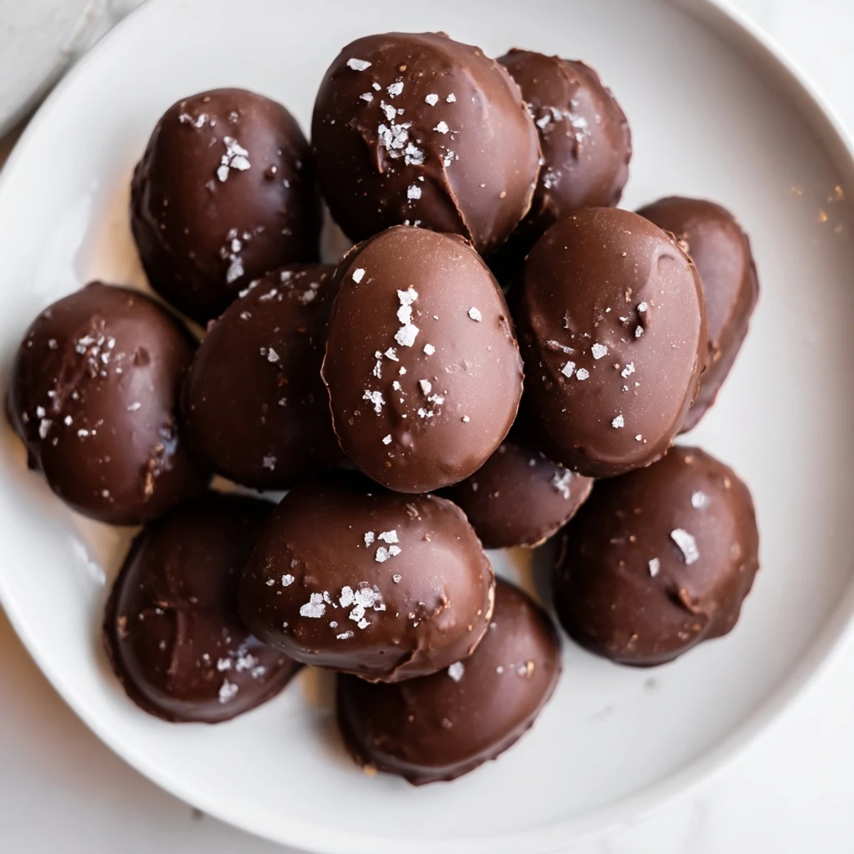 A close-up photo shows a bitten Chocolate Peanut Butter Egg with Sea Salt, revealing a creamy filling and melted chocolate coating on a marble surface.