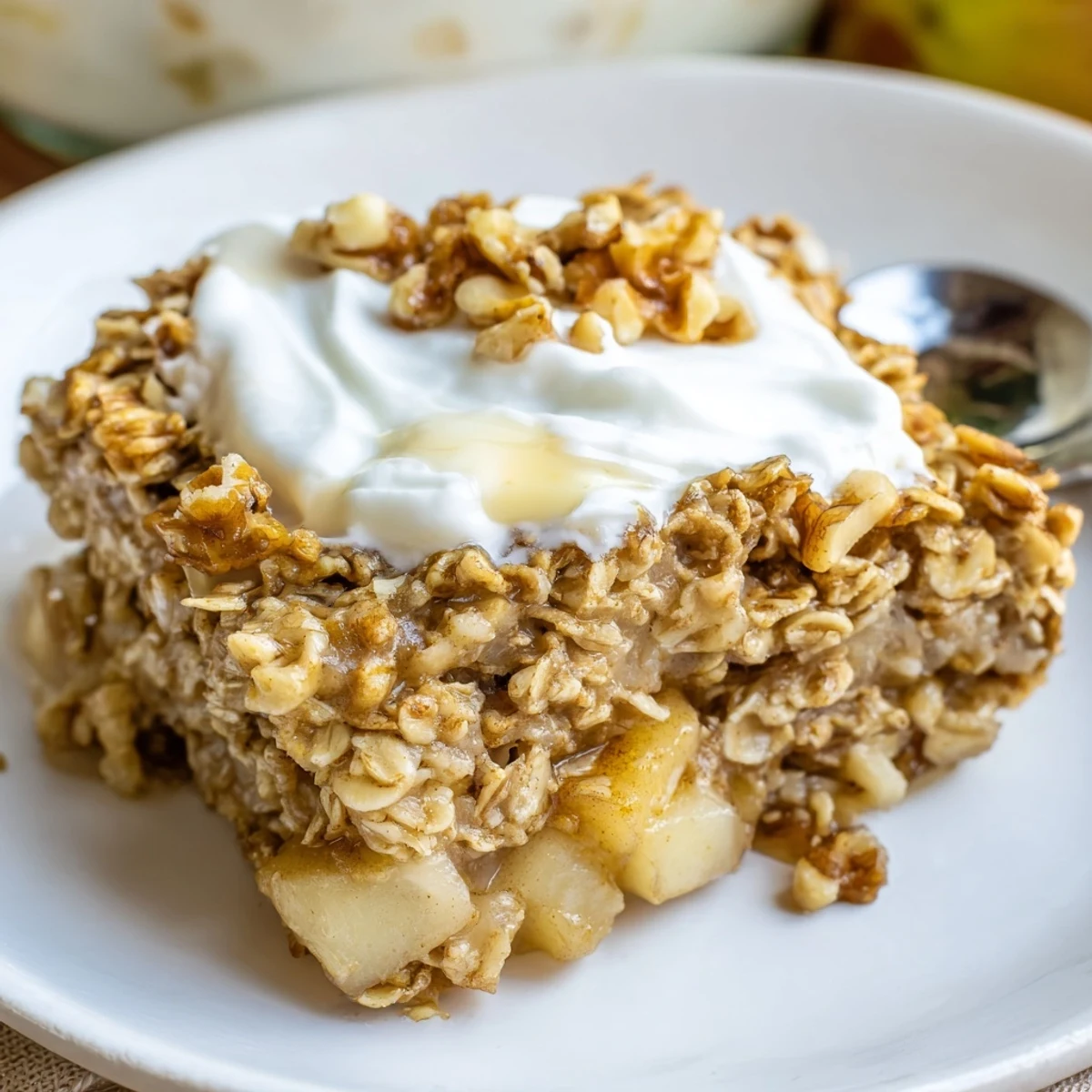 Golden-brown squares of Baked Apple Oatmeal With Greek Yogurt are served on a white plate, topped with creamy Greek yogurt and chopped walnuts for a cozy breakfast.