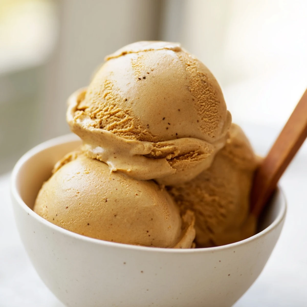 A scoop of Hojicha Ice Cream is served with a drizzle of black sugar syrup on a wooden table.