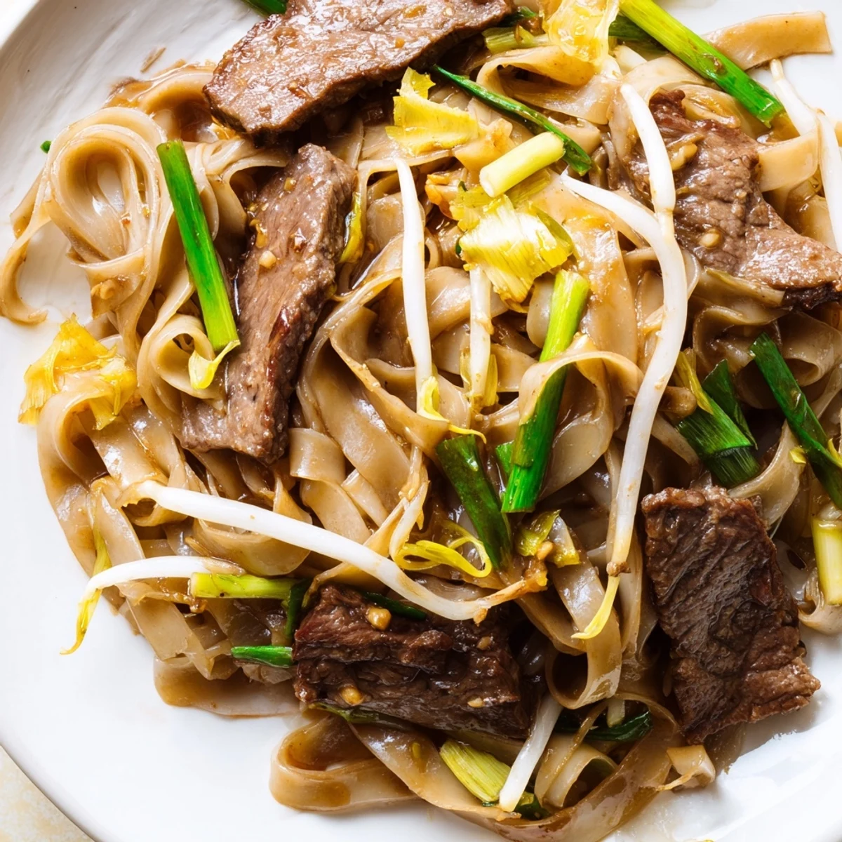 A close view of Beef Chow Fun featuring marinated beef strips alongside spring onions and rich brown sauce.