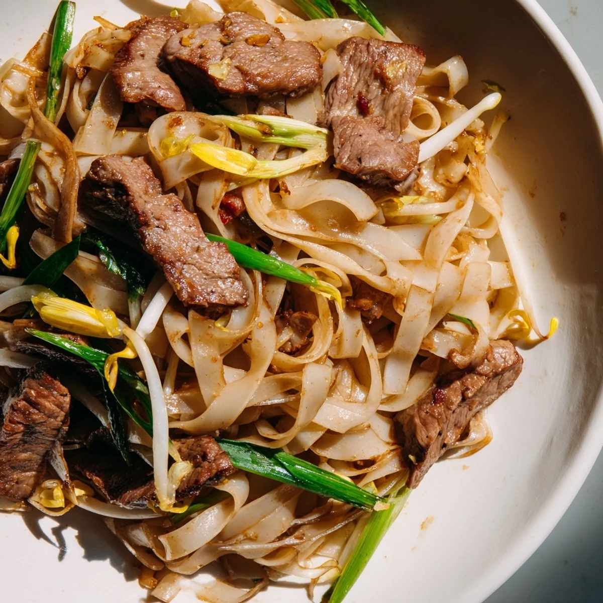 Beef Chow Fun showing glossy noodles seared in wok with caramelized edges and fresh bean sprouts on plate.