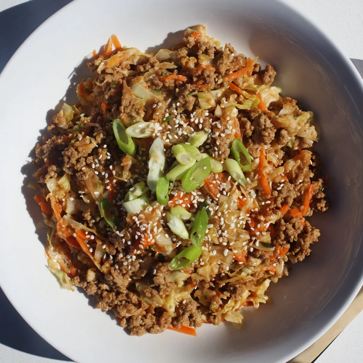 A close-up of savory Egg Roll In A Bowl served in a white bowl, topped with sesame seeds and fresh green onions.