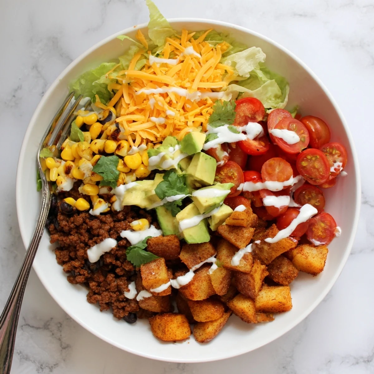 Golden crispy roasted potatoes topped with seasoned taco beef, melted cheddar, and a generous drizzle of lime crema in a vibrant bowl.