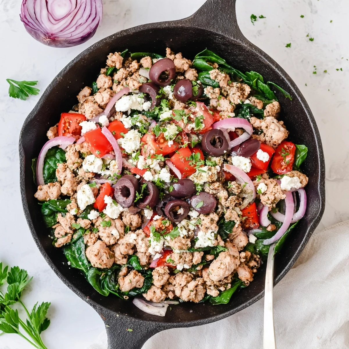 A close-up of Mediterranean Keto Skillet with Ground Chicken, Olives & Feta bubbling in a cast-iron pan with fresh parsley garnish.  