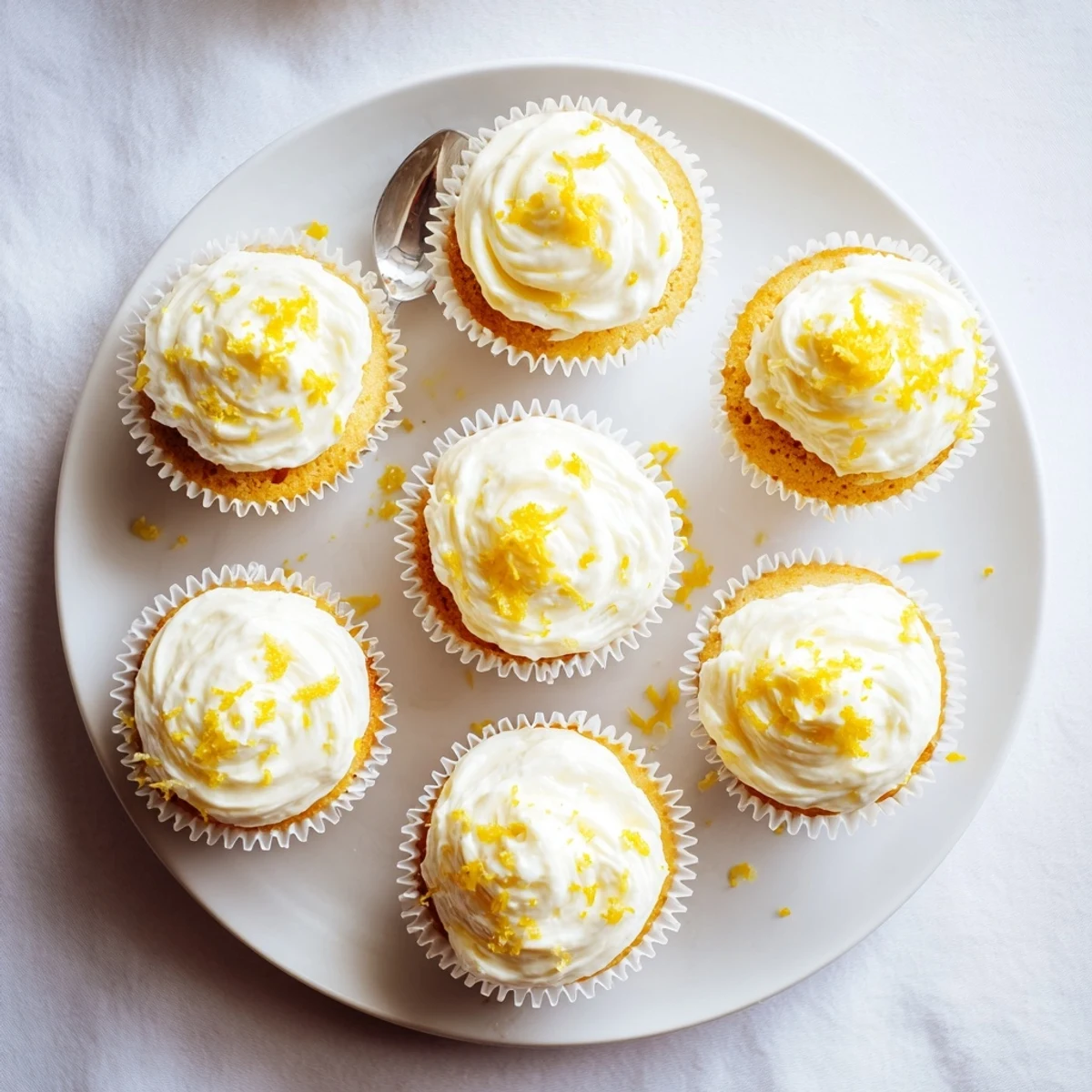 A single Limoncello Cupcake on a white plate displays moist crumb, creamy frosting, and a lemon slice garnish.