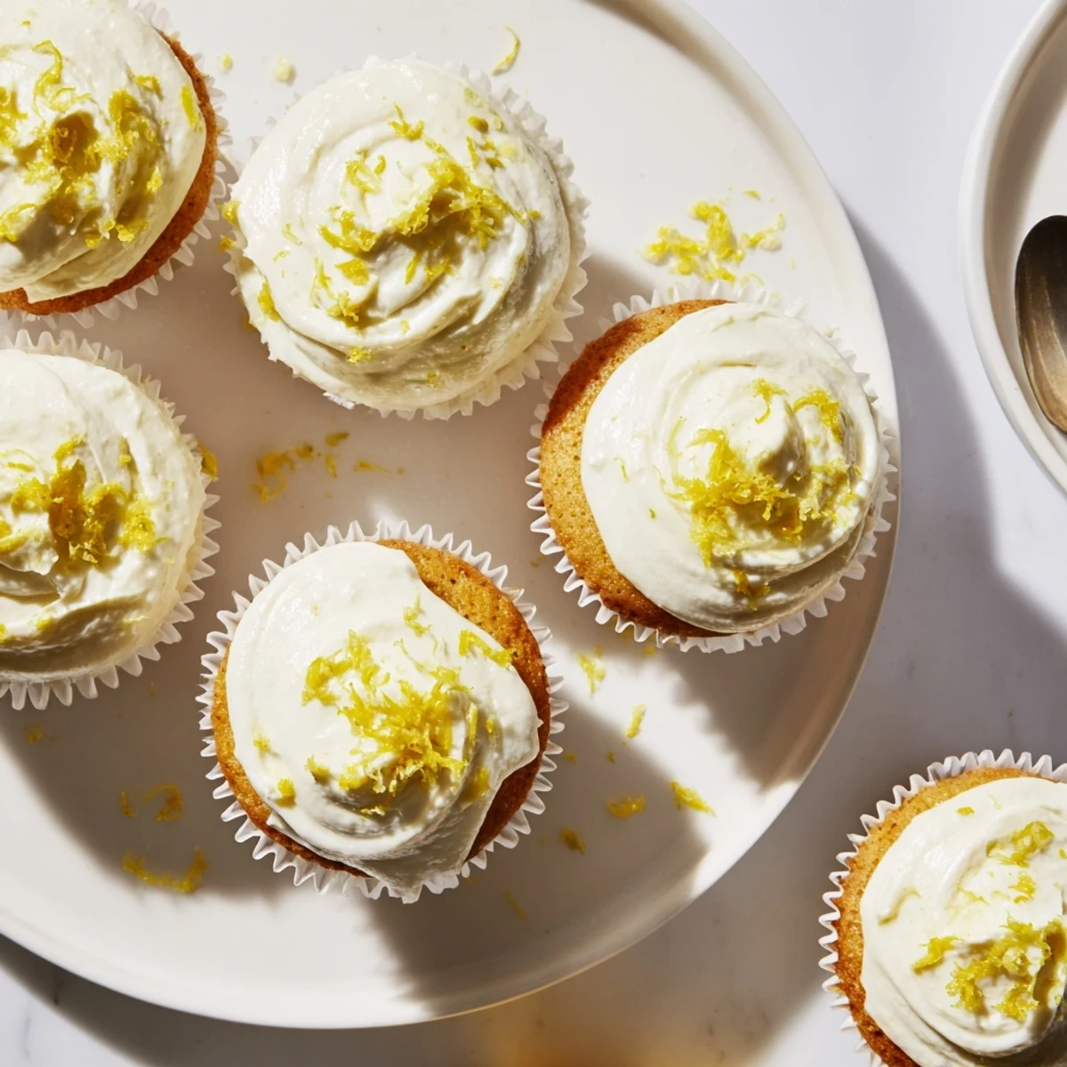 A batch of freshly baked Limoncello Cupcakes shines under warm light, perfect for spring gatherings or summer dessert parties.