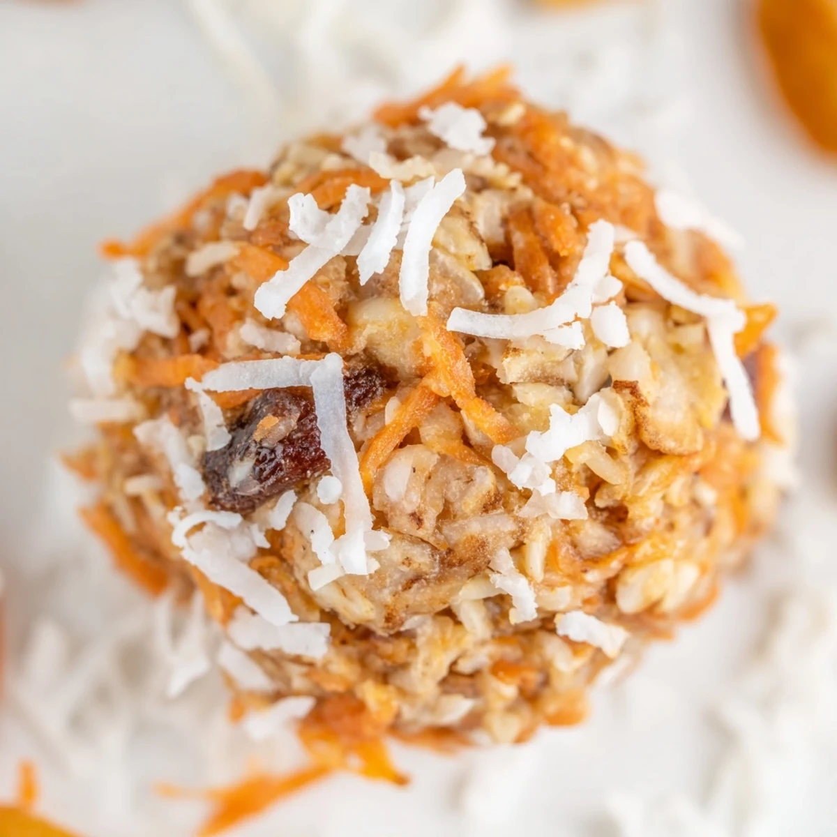Freshly rolled No Bake Carrot Cake Bites with shredded carrots and walnuts on a wooden board.  