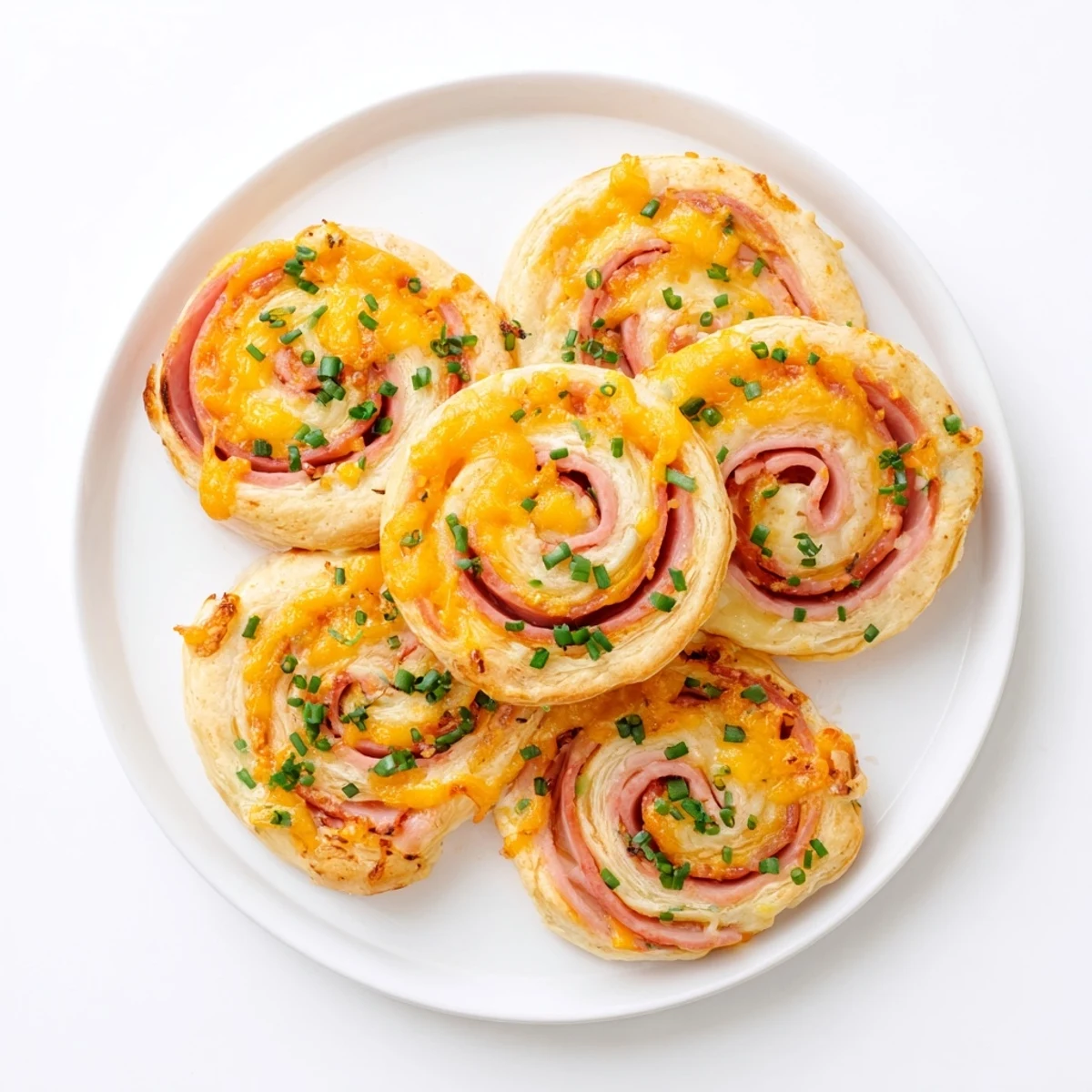 Golden brown Easter Ham Cheddar Pinwheels featuring flaky puff pastry spiraled with smoky ham and melted sharp cheddar cheese on a white serving platter