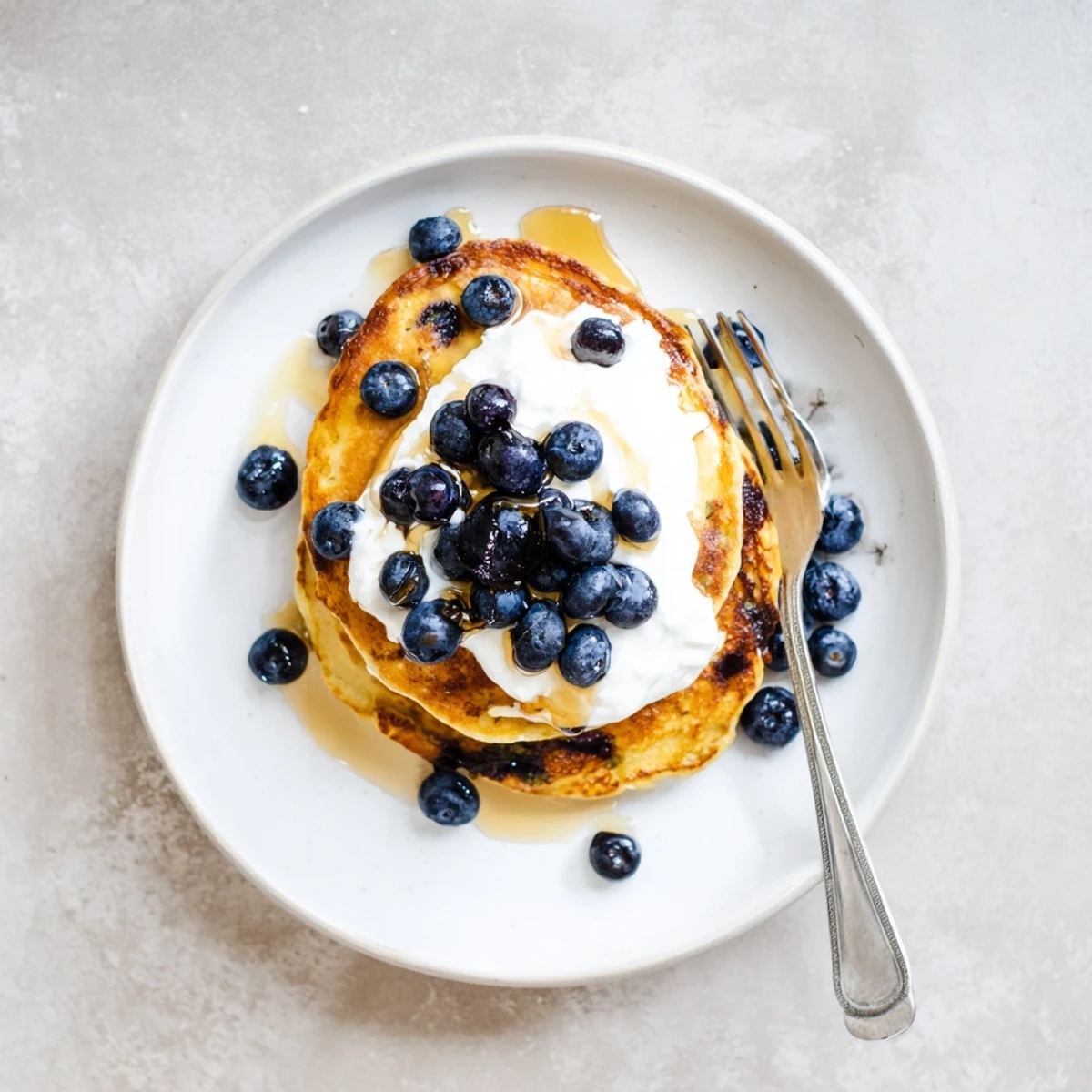 Golden stack of fluffy Greek yogurt blueberry pancakes topped with fresh berries and maple syrup