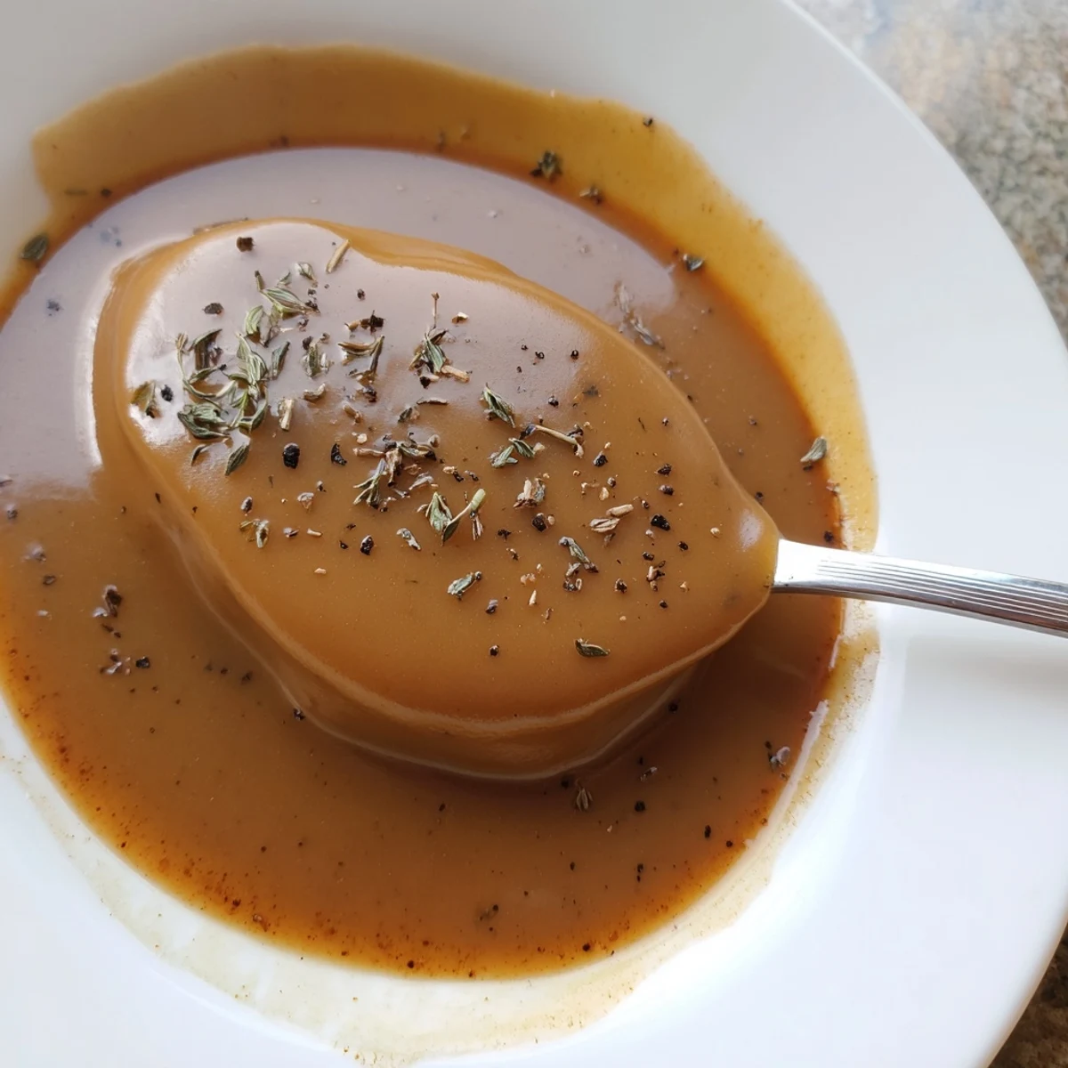 Golden homemade gravy ladled over fluffy mashed potatoes in a white ceramic bowl