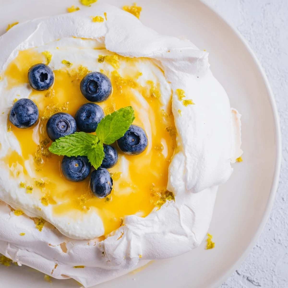 Airy baked meringue nests holding tangy citrus curd with colorful berry garnish on white plate