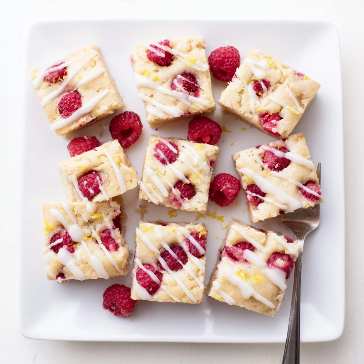 Soft chewy blondies dotted with bright red raspberries topped with tangy lemon icing