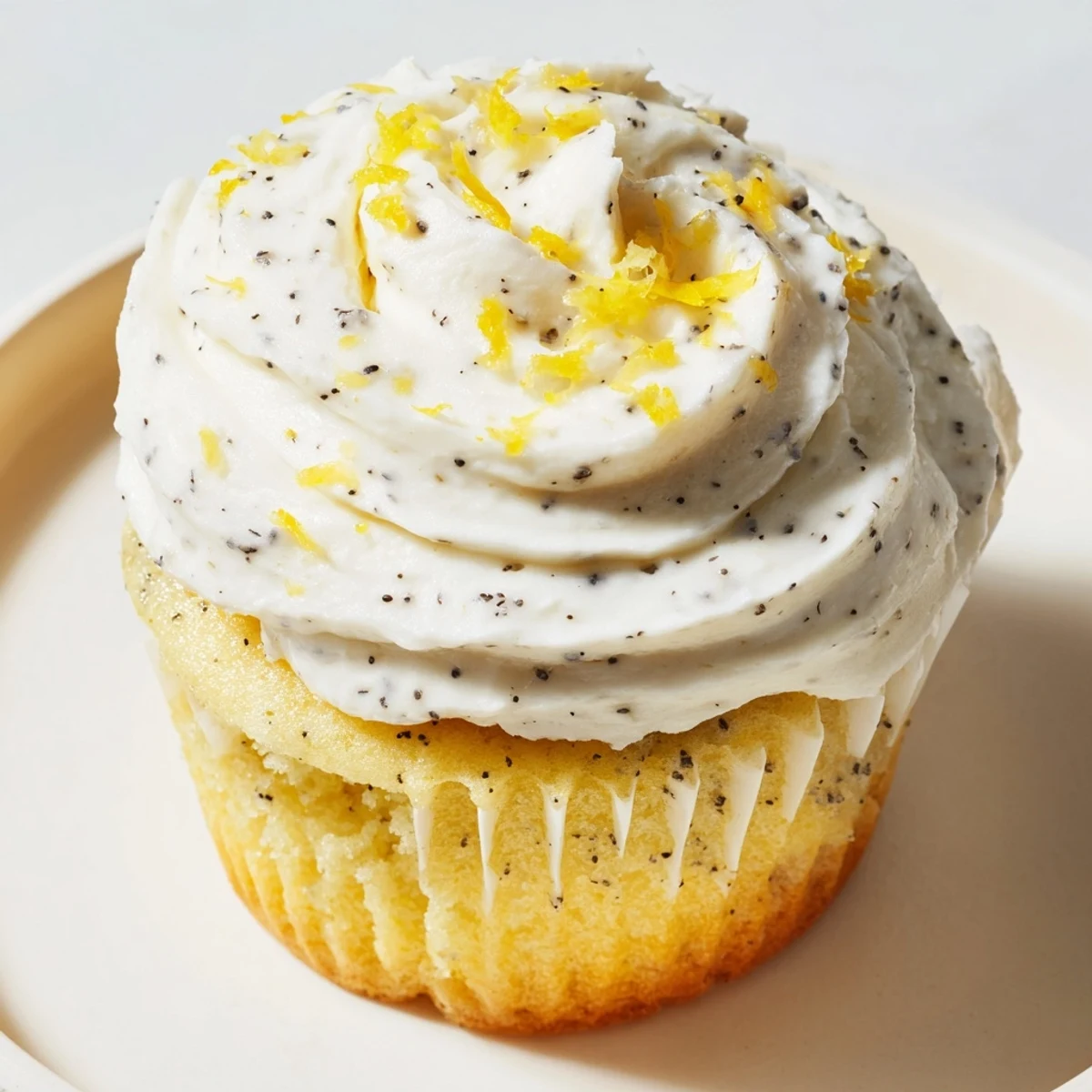 Golden lemon poppy seed cupcakes topped with swirls of creamy lemon frosting on a white plate
