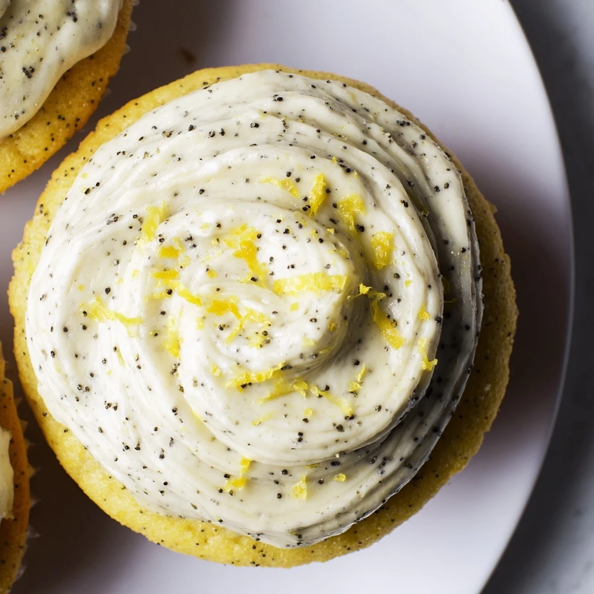 Moist lemon poppy seed cupcakes piped with tangy cream cheese frosting and garnished with lemon zest