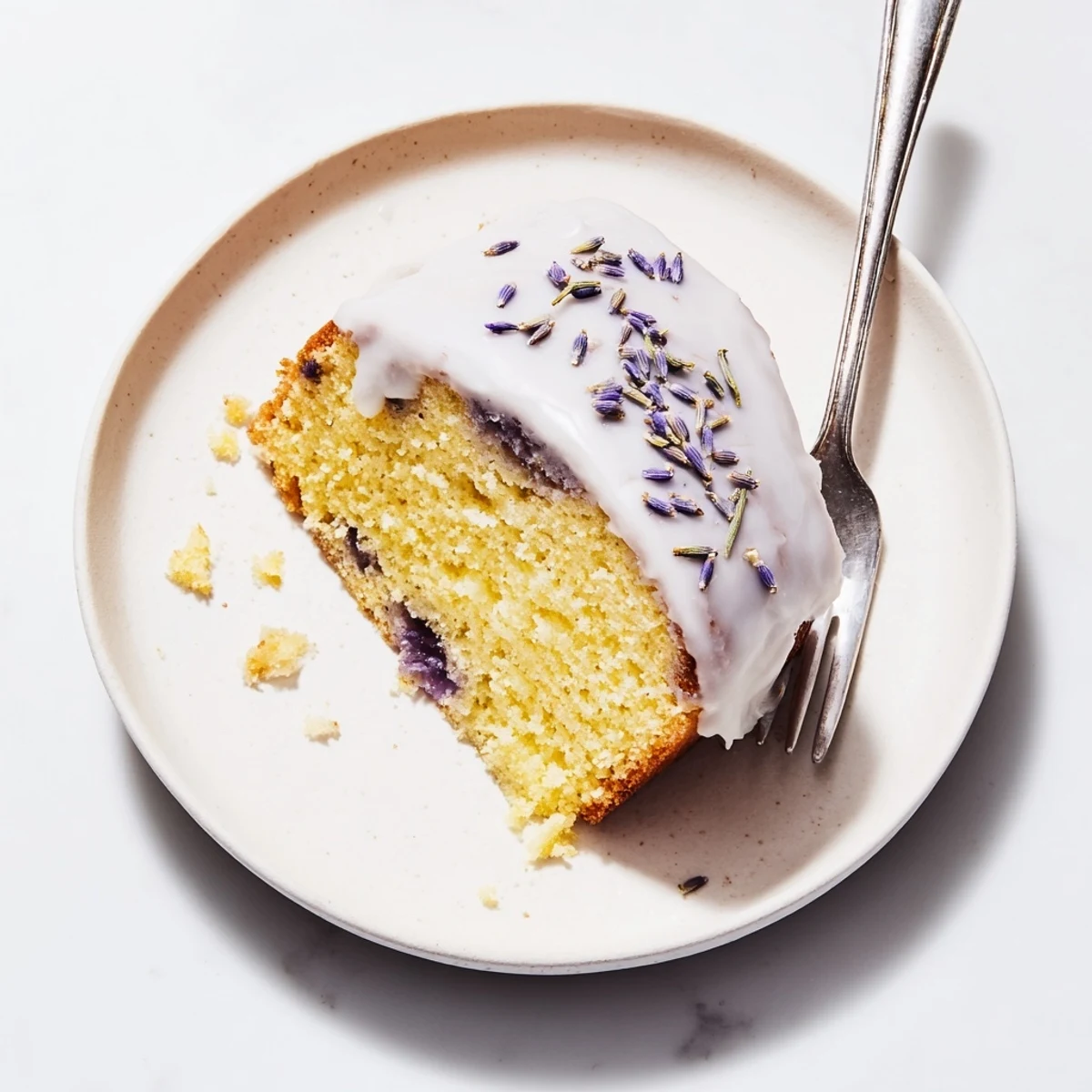 Golden Lemon Lavender Cake drizzled with white glaze and sprinkled with dried purple lavender buds on a white serving plate