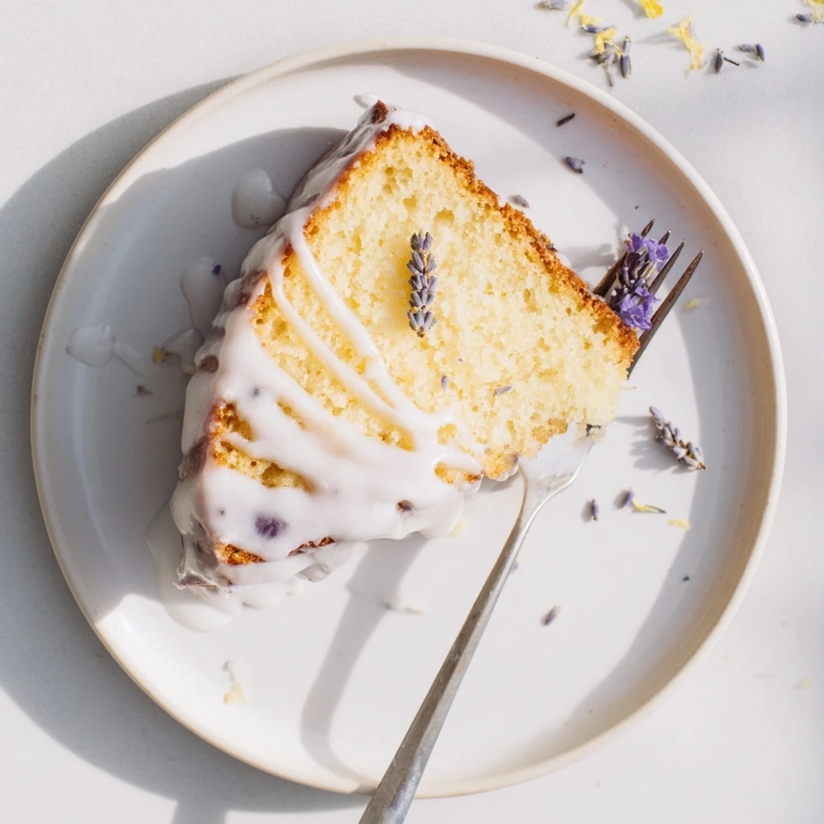 Moist Lemon Lavender Cake slice revealing tender yellow crumb topped with tangy lemon icing and garnished with culinary lavender flowers
