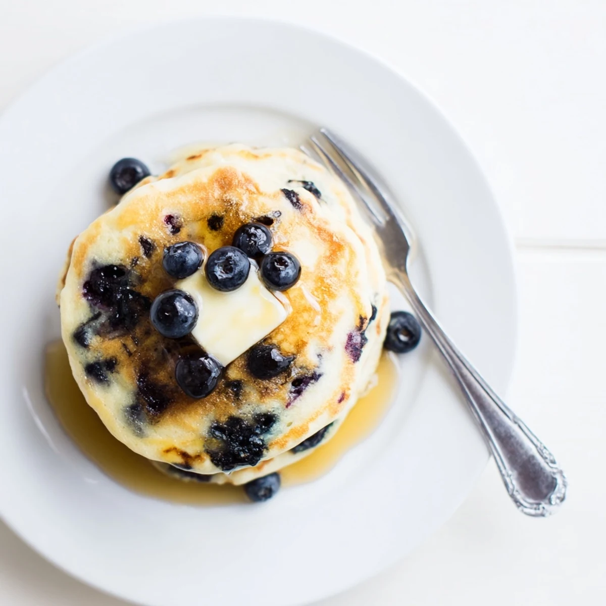 Light and airy Greek yogurt blueberry pancakes served on a wooden board with sweet syrup and scattered fresh fruit
