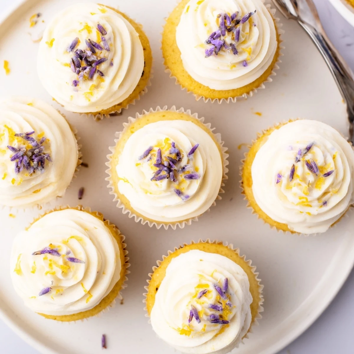 Tender lemon lavender cupcakes piped with lemon buttercream and sprinkled with culinary lavender on a white plate