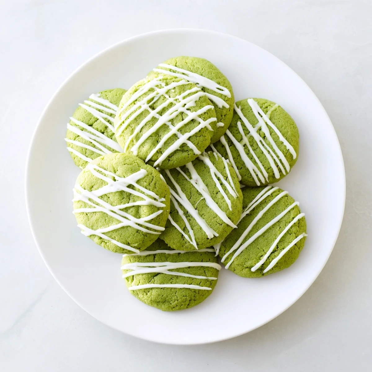 Soft green velvet cookies topped with creamy white chocolate drizzle on a white plate.