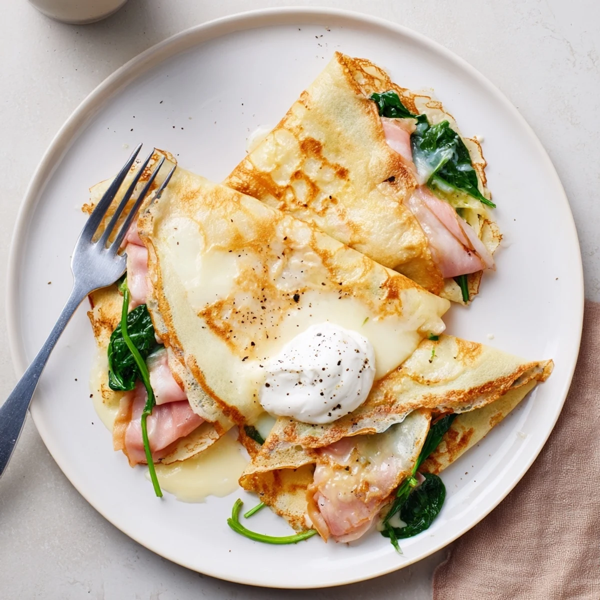 Delicate breakfast savory crepes topped with crème fraîche and black pepper garnish