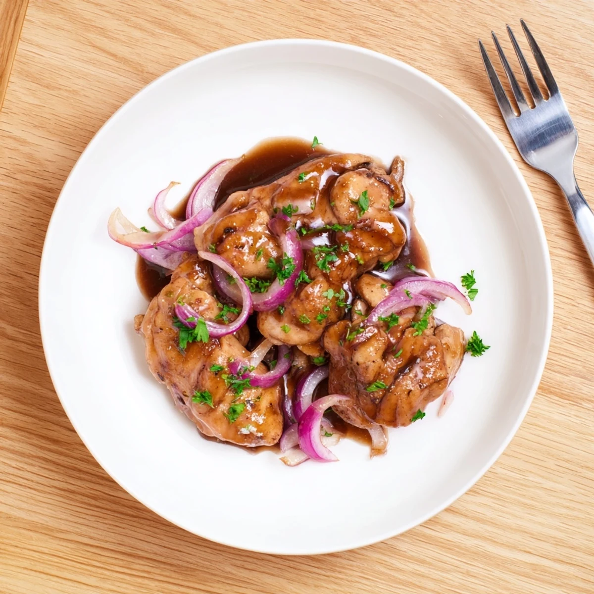 Tender chicken thighs simmering in tangy balsamic vinegar sauce with caramelized red onion slices