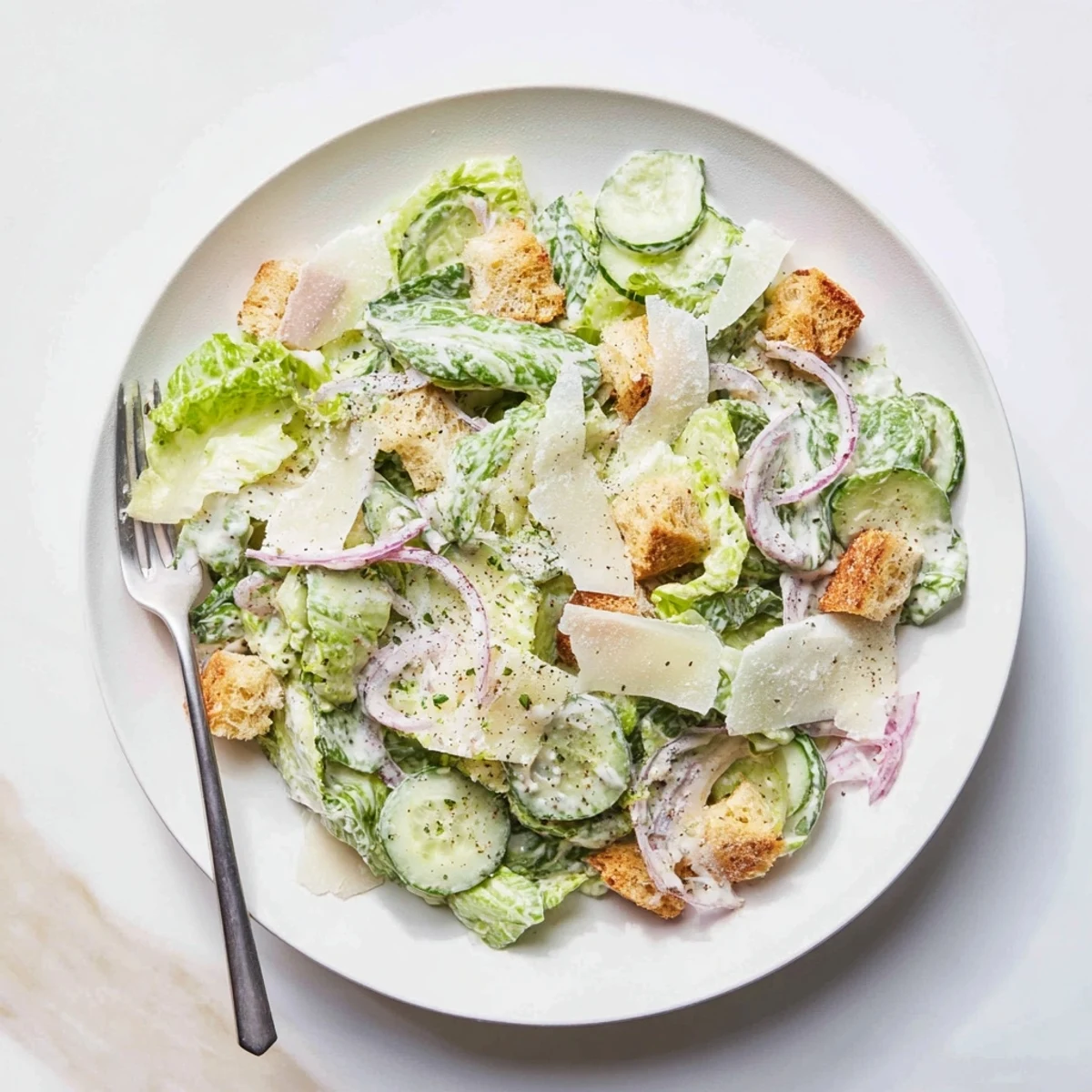 Vibrant bowl of cucumber Caesar salad topped with homemade dressing, shaved cheese, and buttery toasted croutons