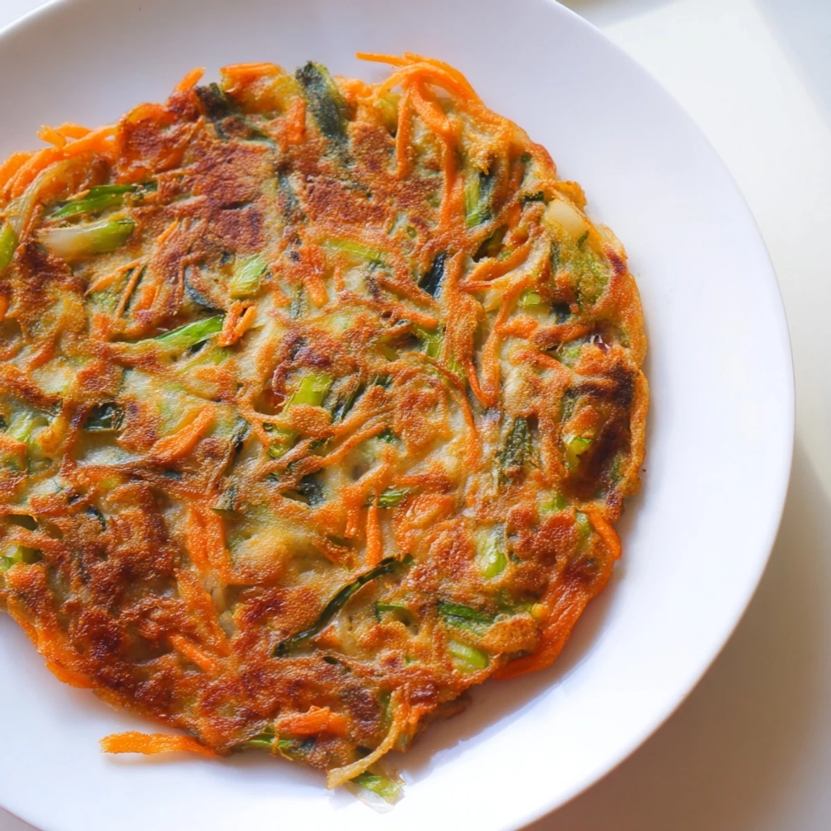 Golden brown crispy Korean pancakes loaded with fresh scallions and colorful vegetables on a white plate