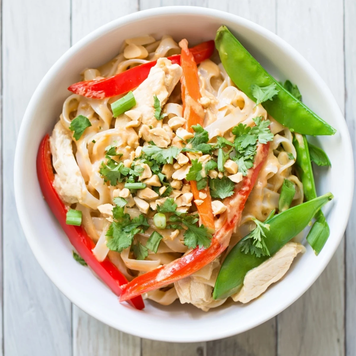 Golden chicken and crisp vegetables smothered in rich peanut sauce for Thai peanut chicken noodle bowls