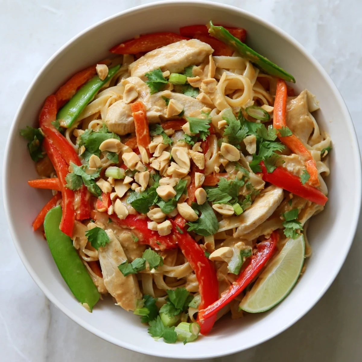 Vibrant stir-fried vegetables and chicken coated in glossy peanut sauce served over rice noodles