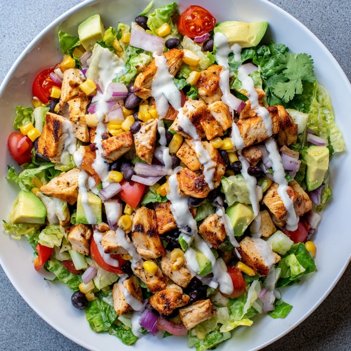 Vibrant healthy BBQ chicken chopped salad arranged in a bowl with romaine, tomatoes, and tangy yogurt dressing