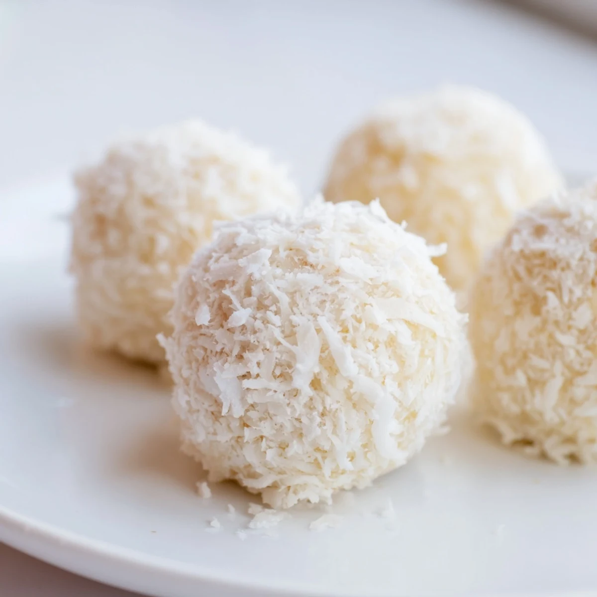 White coconut no bake Easter bunny tails dusted with powdered sugar on a festive pastel serving plate