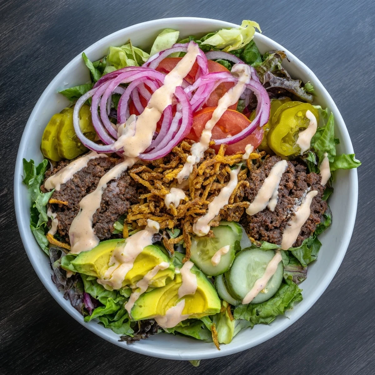 Golden crispy smash burger patties served over fresh greens with pickles and creamy sauce in a deconstructed bowl