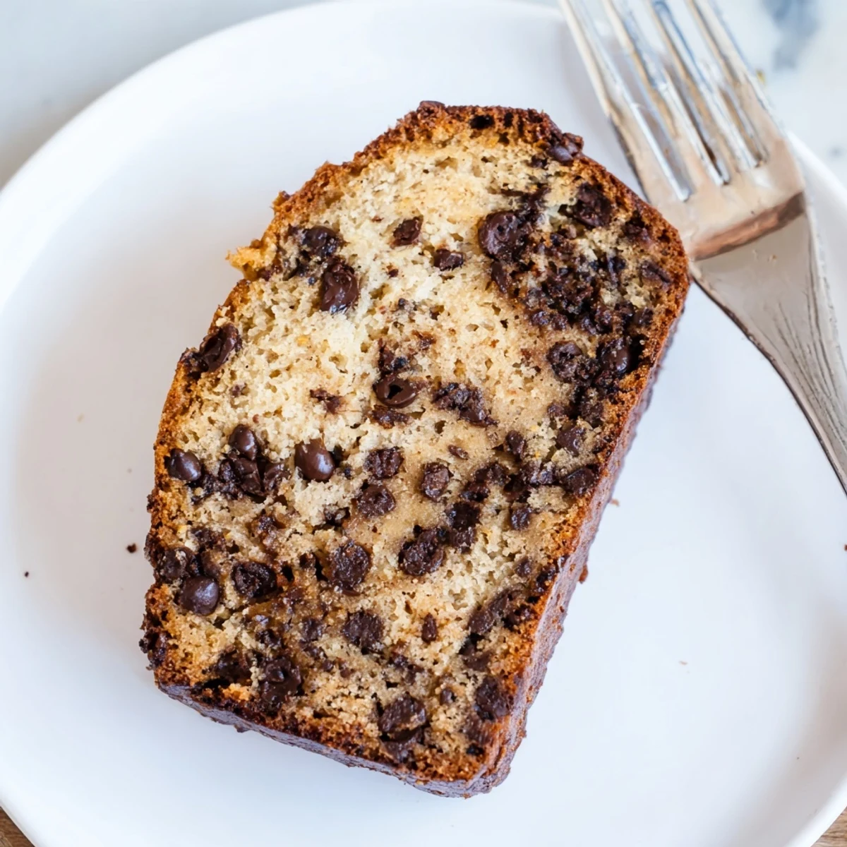 Golden chocolate chip banana bread loaf sliced on a wooden cutting board with melted chips visible
