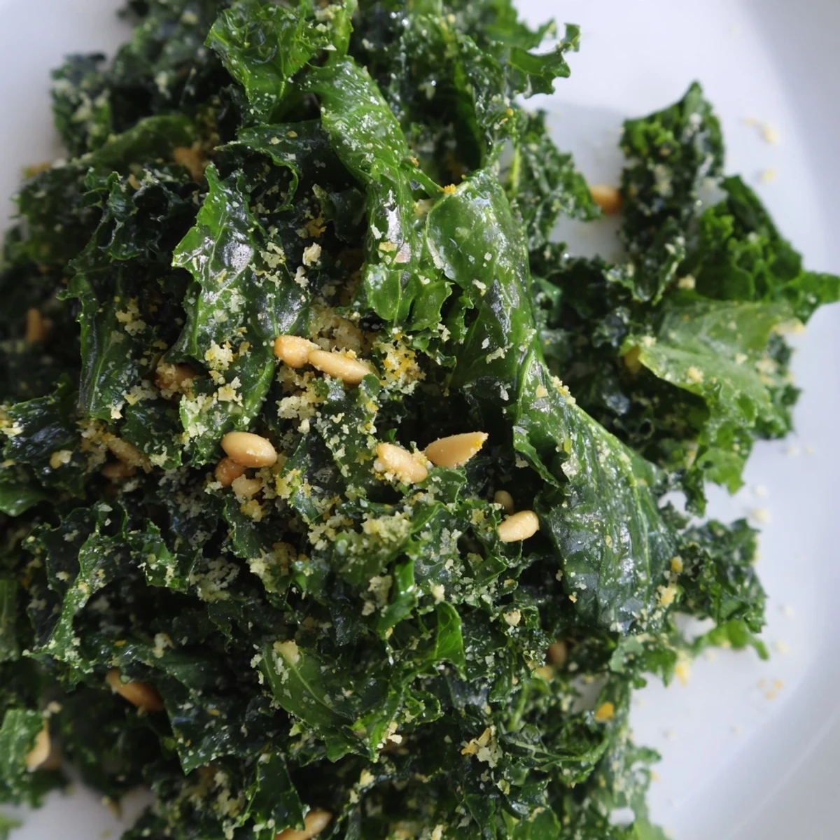 Garlic Lemon Parmesan Kale Salad in a white bowl with shaved cheese and toasted nuts