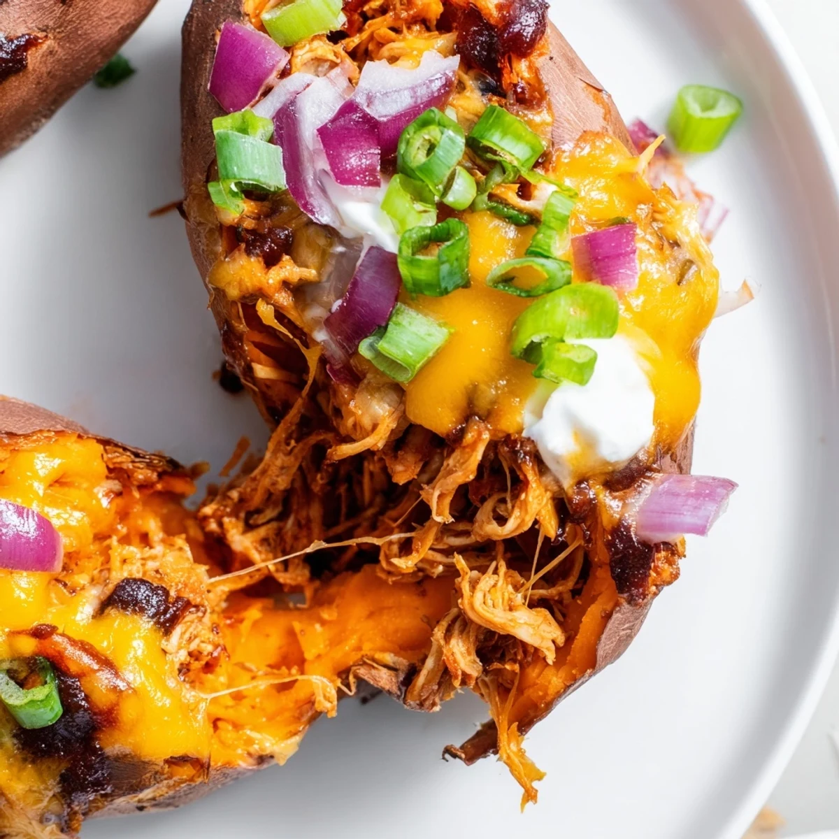 BBQ chicken stuffed sweet potatoes loaded with tangy barbecue sauce and gooey cheese on a white plate