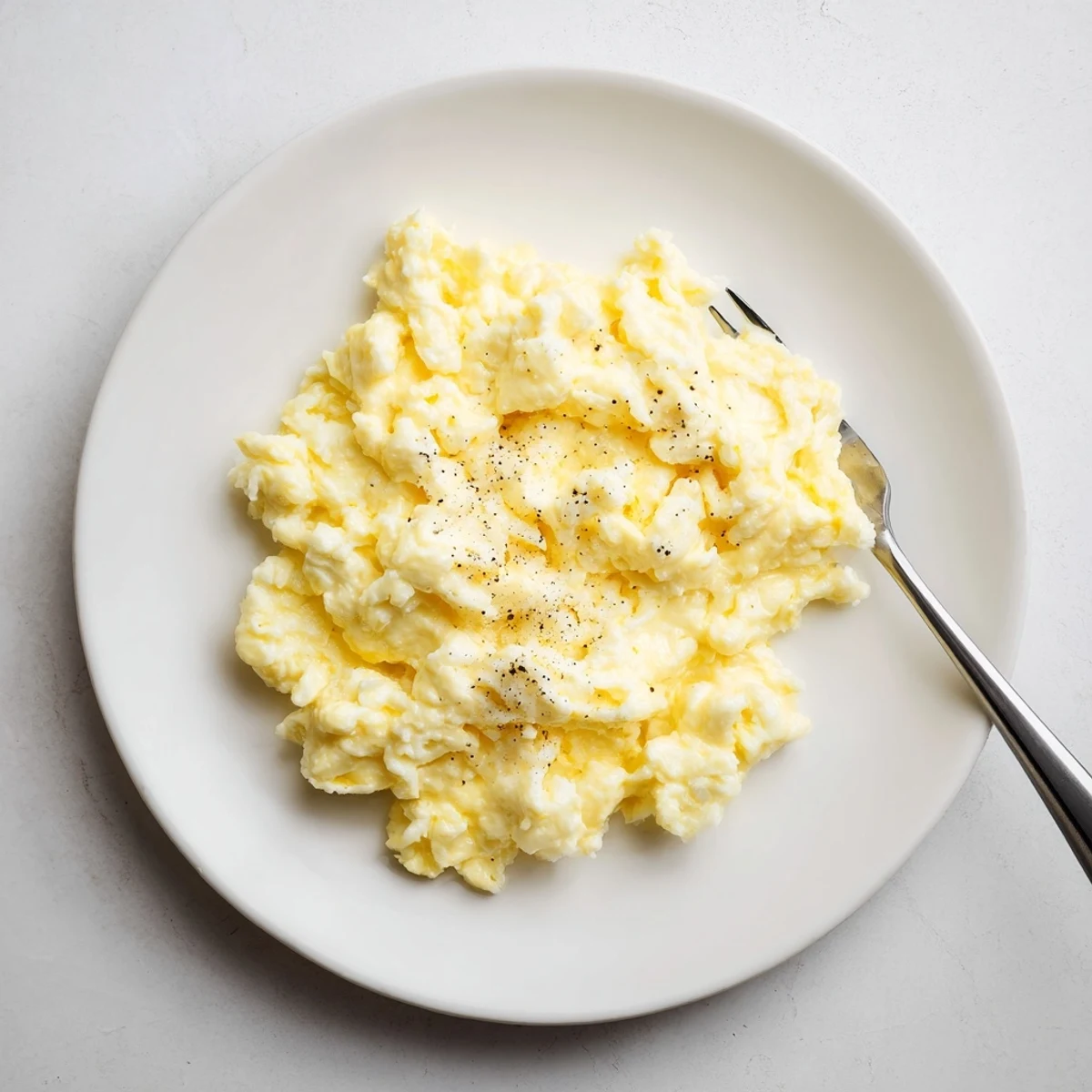 Rich scrambled eggs seasoned with pepper served alongside toasted bread and avocado