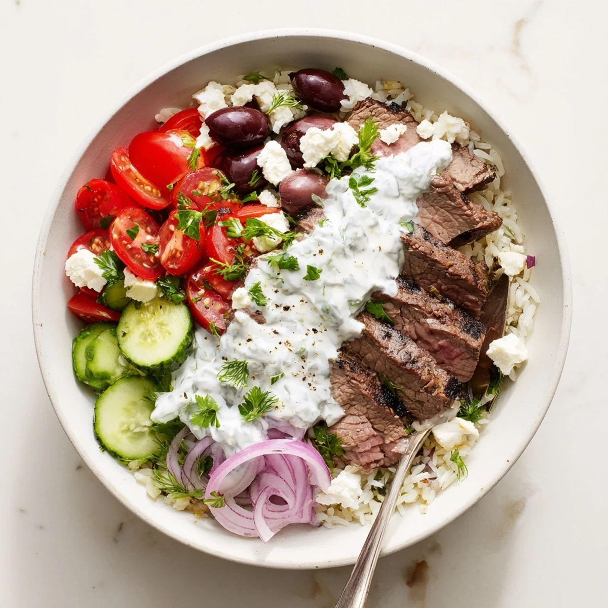 Vibrant Mediterranean steak bowl with juicy spiced steak, fresh tomatoes, cucumbers, olives, and creamy yogurt sauce