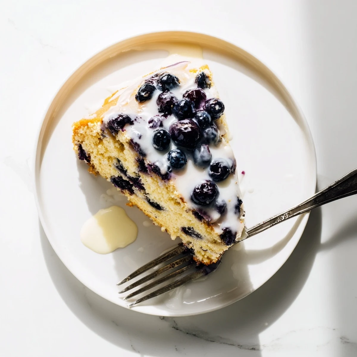 Golden slice of lemon blueberry cake on a white plate with powdered sugar dusting