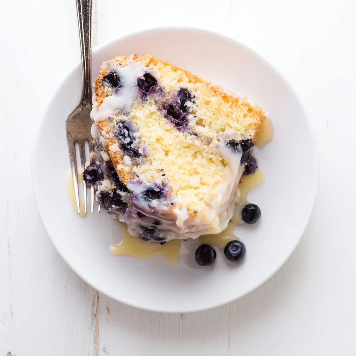 Moist lemon blueberry cake drizzled with white glaze and topped with fresh berries
