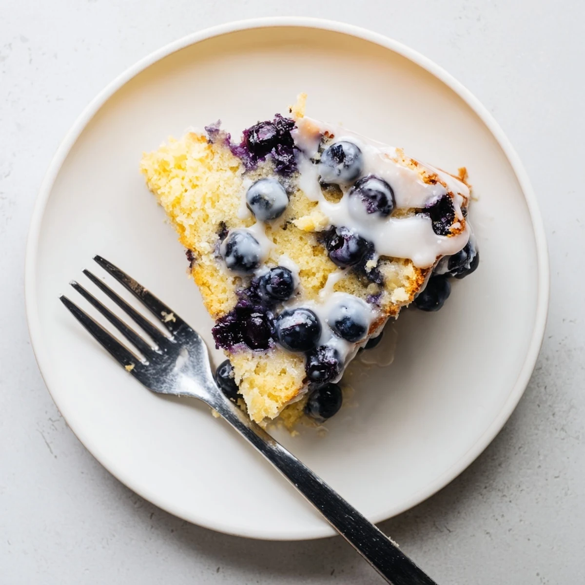 Bundt cake studded with purple blueberries and bright lemon zest on wooden serving board