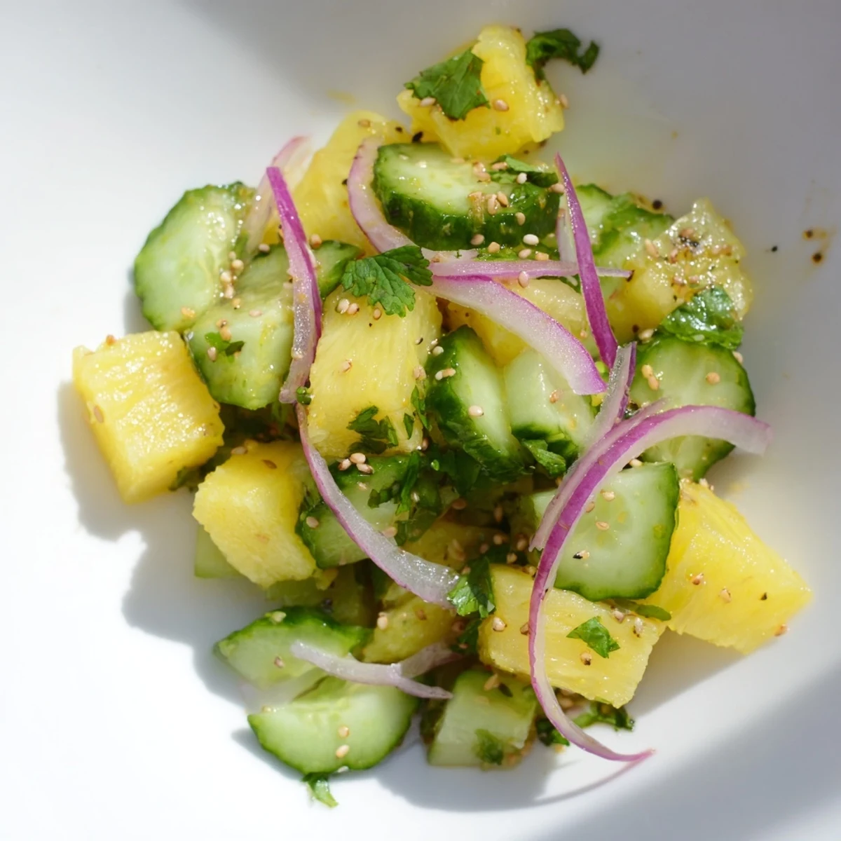 Vibrant pineapple cucumber salad topped with sesame seeds and fresh chili slices on a rustic wooden table