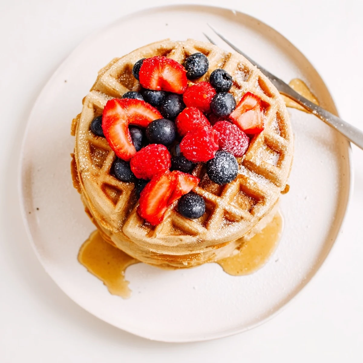 Warm Almond Flour Waffles With Berries topped with powdered sugar and maple syrup