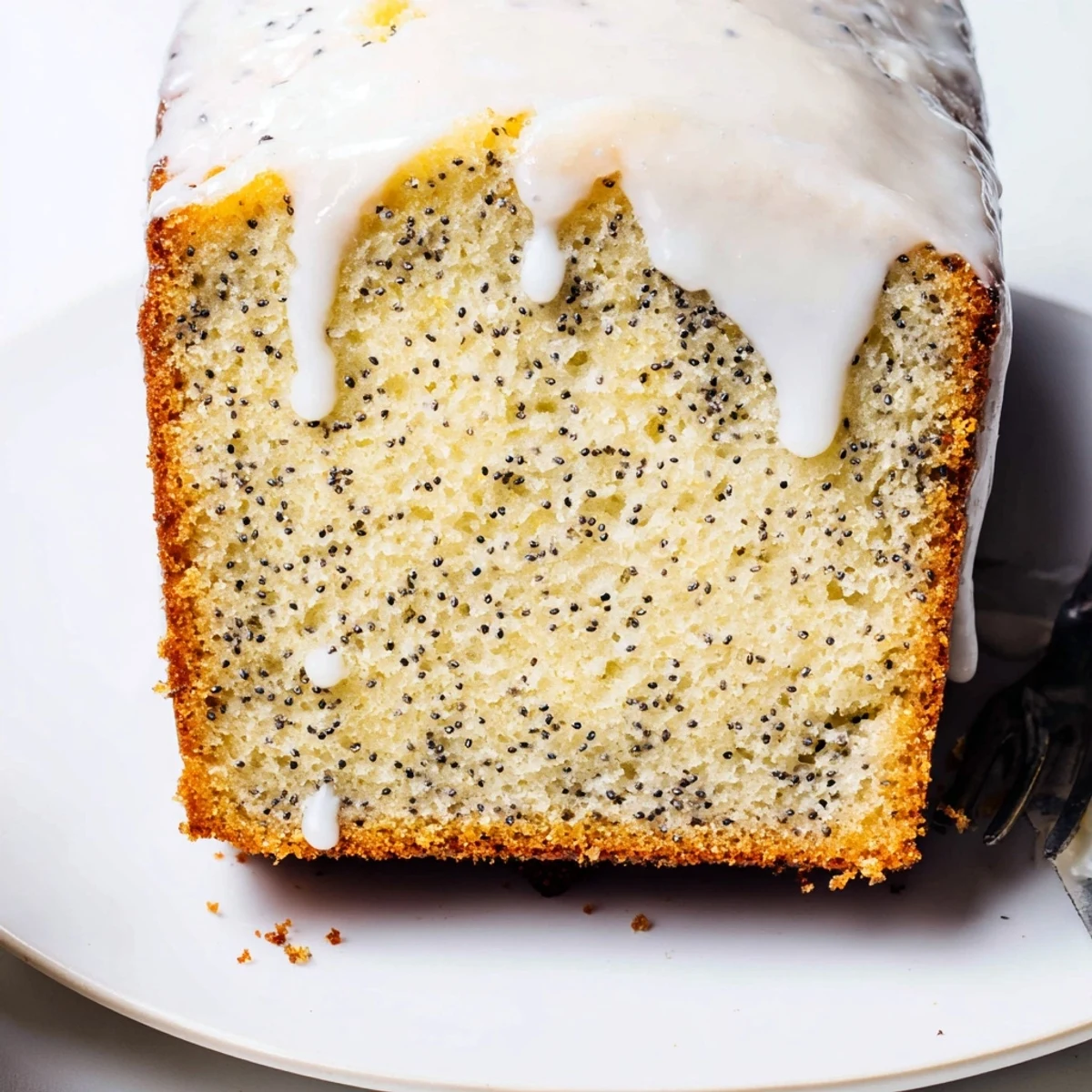 Moist zesty lemon poppy seed cake slice with poppy seed crumb on white plate